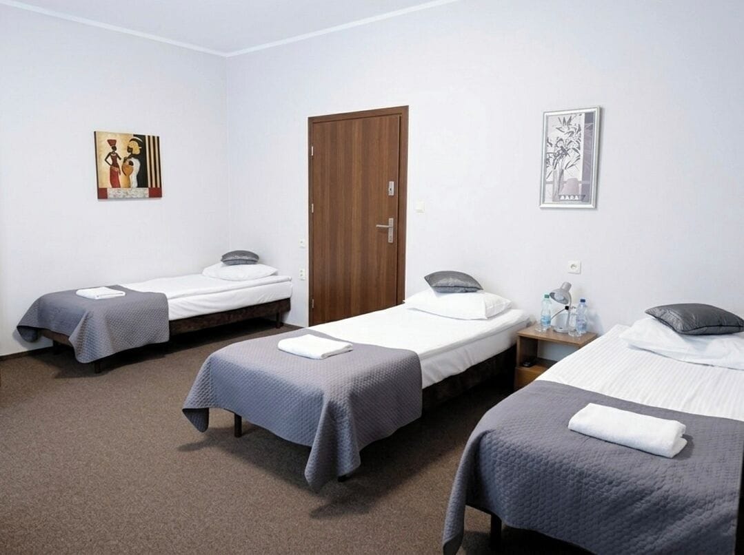 A hotel room with three single beds, a wooden door, and two wall art pieces.