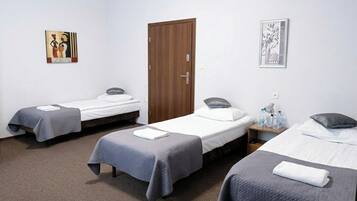 A hotel room with three single beds, a wooden door, and two wall art pieces.