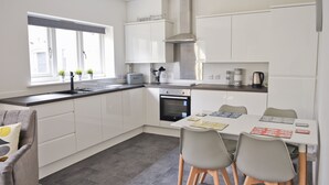 A modern kitchen with white cabinets, a stainless steel range hood, a built-in oven, and a dining area with a table and chairs. - Toothbrush Apartments - Central Ipswich - Fore St - Adults Only (Ipswich)