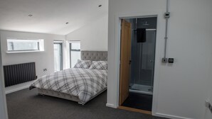 A bedroom with a bed, a radiator, a window, and a door leading to a shower area. - Toothbrush Apartments - Central Ipswich - Fore St - Adults Only (Ipswich)