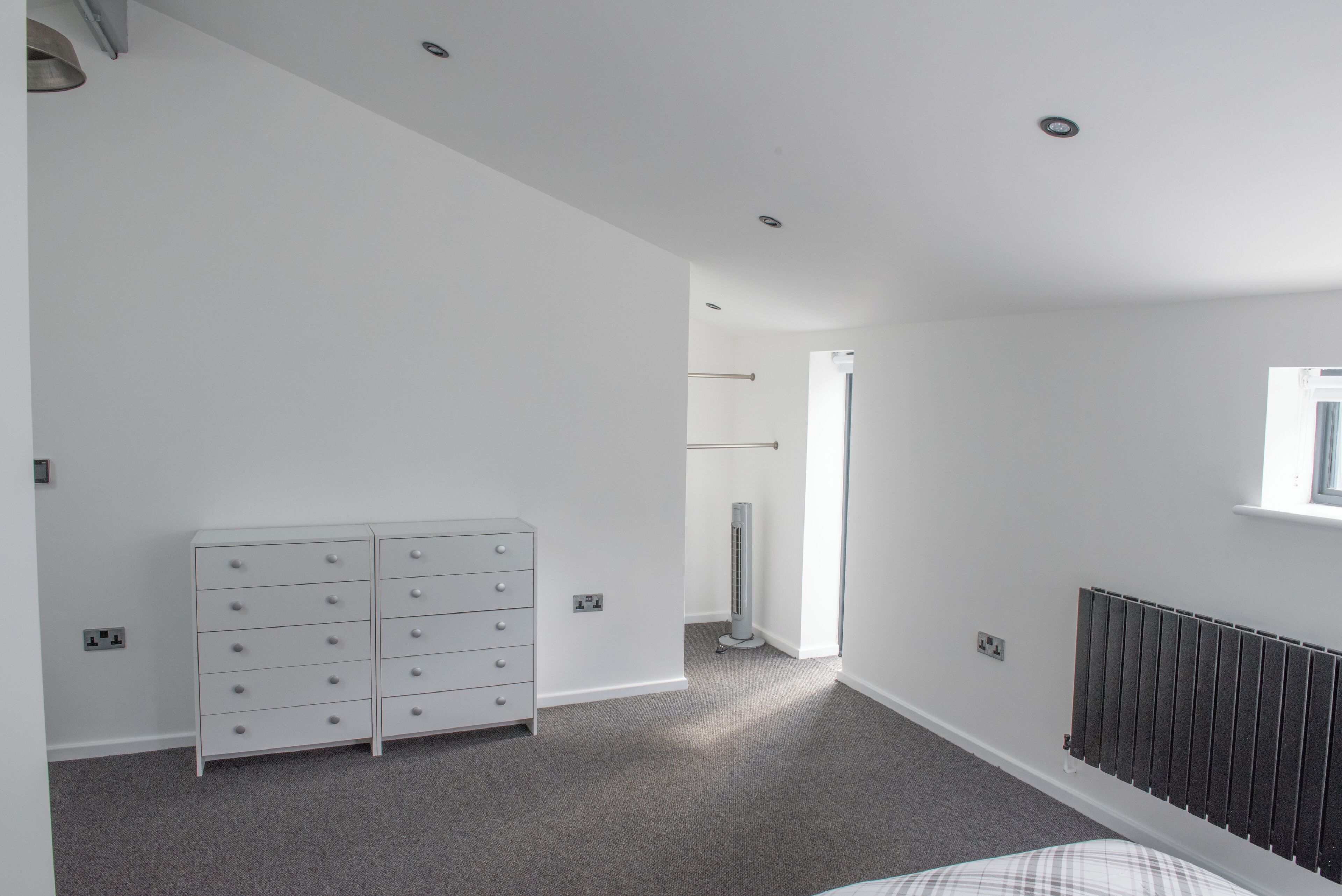 Une chambre avec une commode blanche, un radiateur et une fenêtre laissant entrer la lumière naturelle.