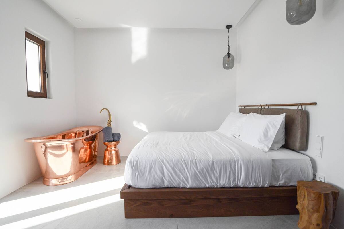 Quarto moderno com cama de madeira, banheira de cobre e um pequeno banquinho de madeira.