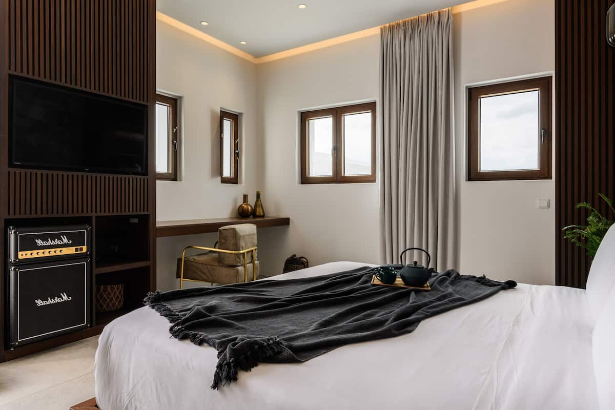 Quarto de hotel moderno com uma cama grande, televisão de tela plana, amplificador Marshall, uma cadeira e uma janela com cortinas.