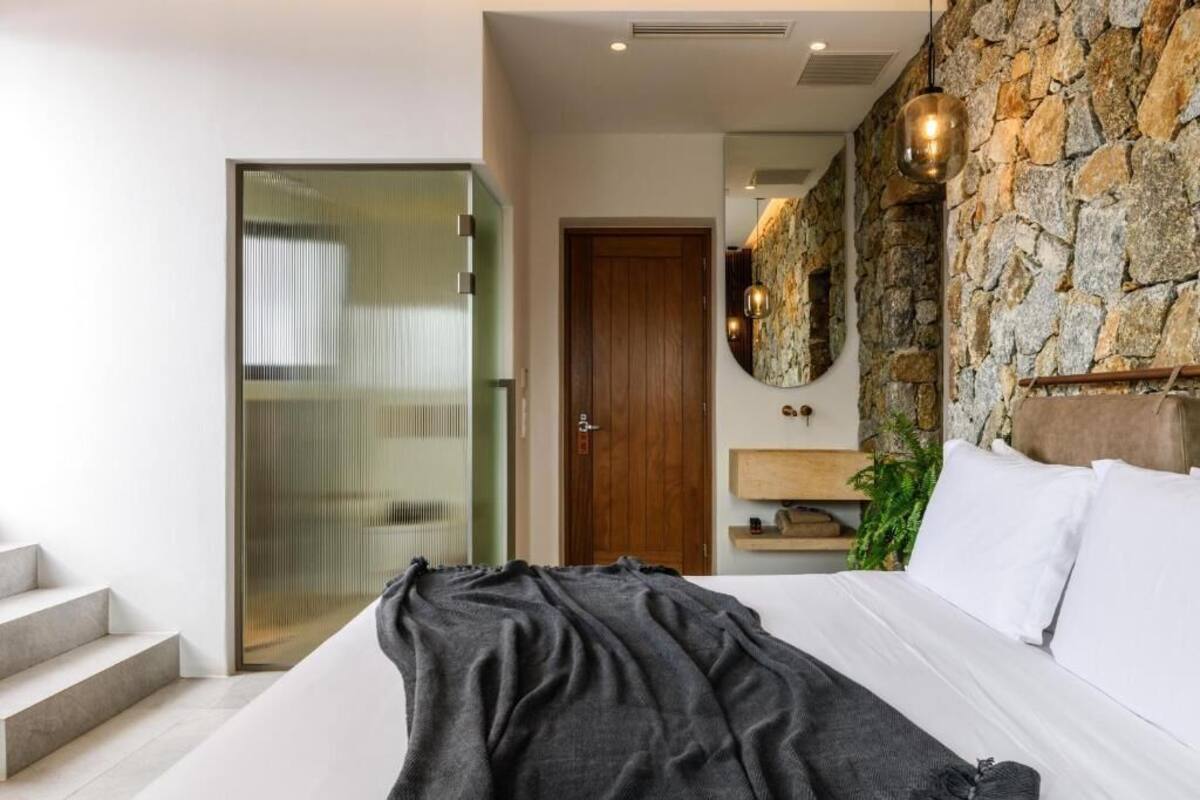 Quarto moderno com cama grande, parede de destaque em pedra, porta de madeira e escada.