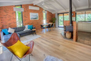 A spacious living area with a brick wall, a sofa, a dining table, and a kitchen area with a stove.