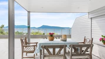 Un espacio de estar al aire libre con techo, con una mesa y sillas, con vistas a un paisaje montañoso y una masa de agua.