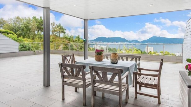 Une terrasse extérieure couverte, dotée d’une table et de chaises, offrant une vue panoramique sur un plan d’eau et des montagnes.