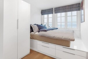 Un dormitorio con cama, armario blanco y ventana con cortinas.
