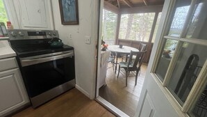 A kitchen with a stove, oven, and a dining area with a table and chairs. - Peaceful lake cottage in rolling hills of Maine (Sumner)