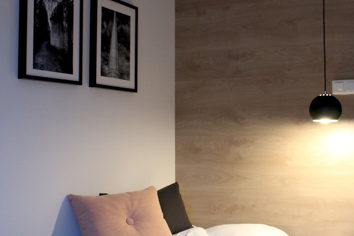 Un dormitorio moderno con cama, dos cuadros enmarcados, una lámpara de noche y un cabecero de madera.
