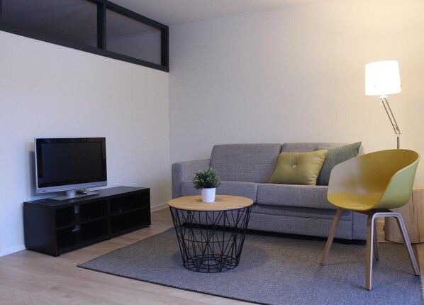 A modern living room with a grey sofa, a yellow chair, a round coffee table with a plant, a TV on a black stand, and a floor lamp.