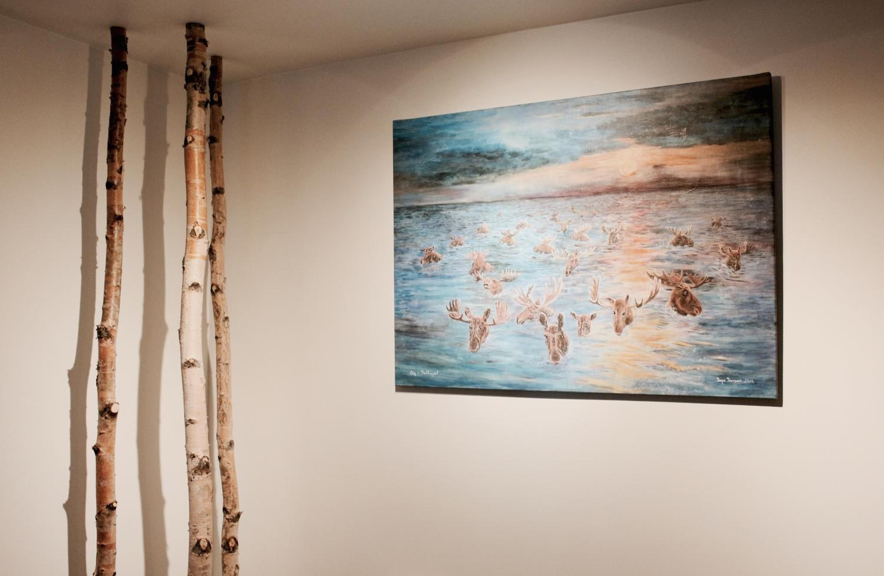 Ein Gemälde von Elchen auf einem Gewässer, eine Wand mit drei vertikalen Holzelementen und eine schlichte Wand.