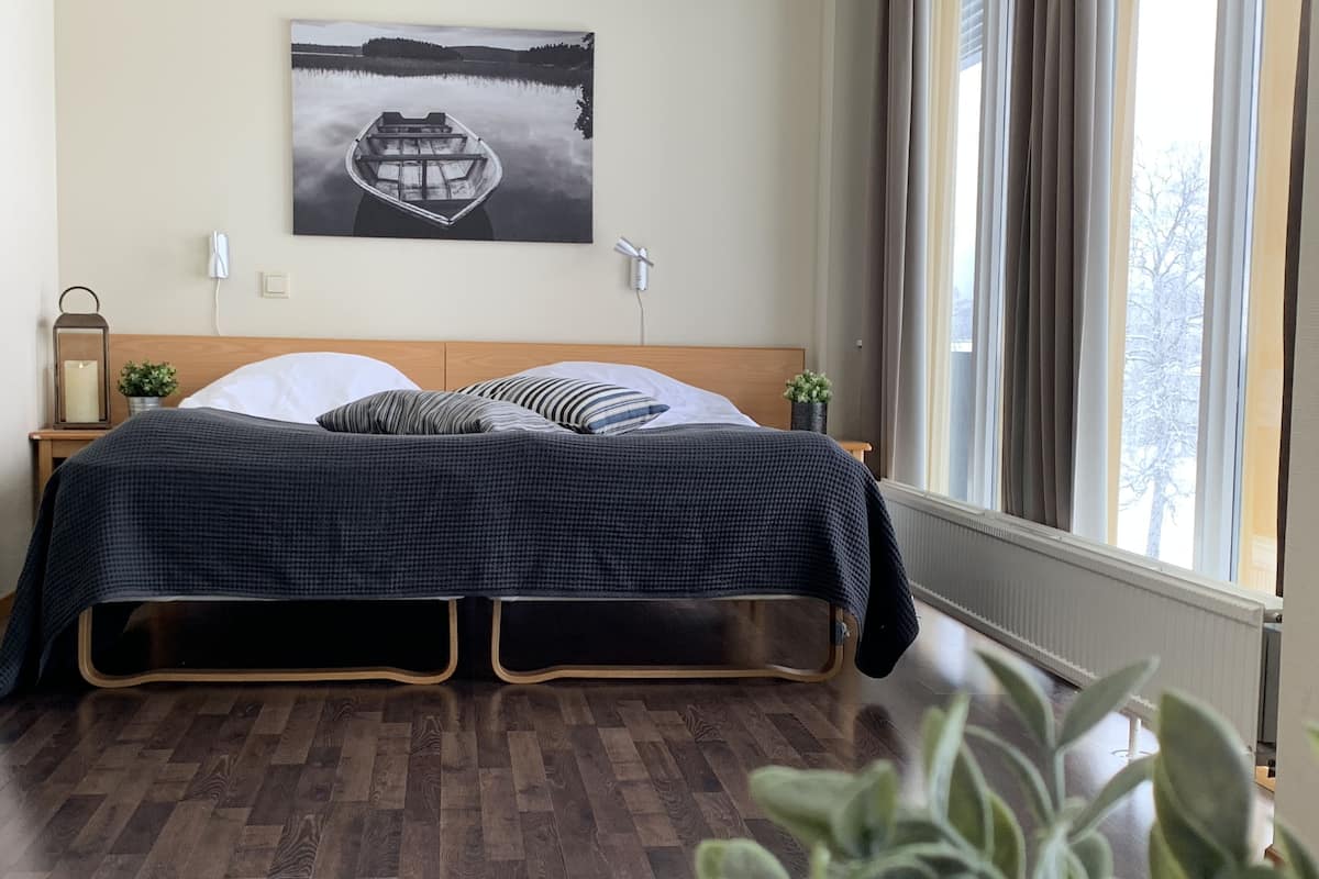 Un dormitorio con una cama de madera, un cuadro blanco y negro en la pared y vistas a árboles desde la ventana.