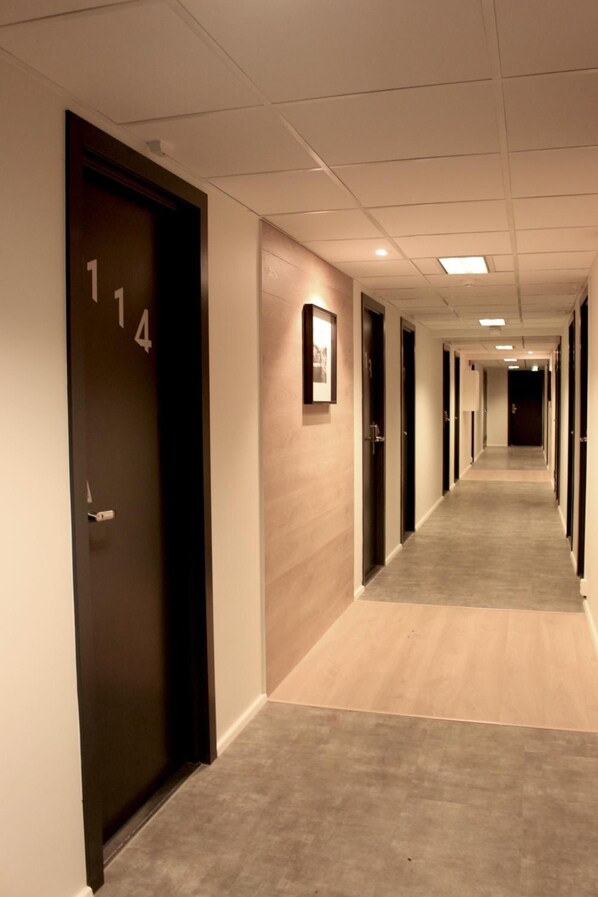 Pasillo de hotel con puertas numeradas 114 y 115, piso alfombrado e iluminación empotrada.