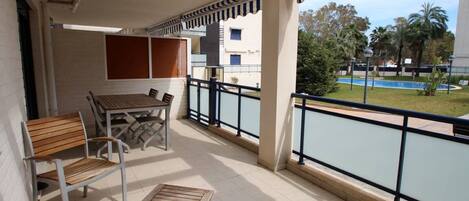 A balcony with a table and chairs, a view of a swimming pool, and a building in the background.