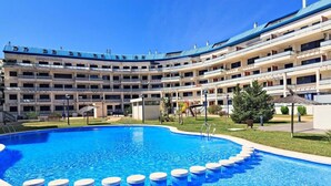 Un hotel con una piscina amplia, varios balcones y un césped bien cuidado.
