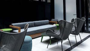 A modern outdoor seating area with a glass ceiling, a sofa, and wicker chairs. - The Draper New York, Tapestry Collection by Hilton (New York)