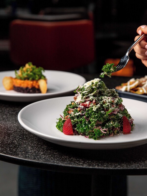 A close-up of a dish with kale, strawberries, and crumbled cheese on a plate.
