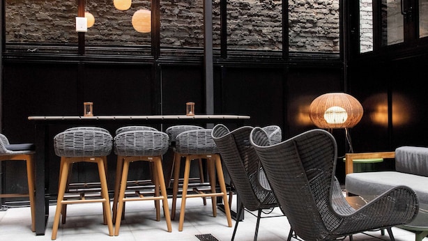A modern interior with a high ceiling, exposed brick walls, and a dining area with wicker chairs and a table. - The Draper New York, Tapestry Collection by Hilton (New York)