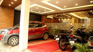 A modern indoor parking area with a red carpet, a red SUV, and a motorcycle. - Grand Oliver (Chennai)