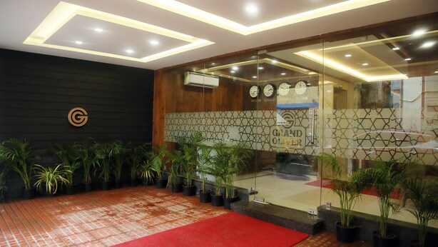 A reception area with a red carpet, potted plants, a wall clock, and a geometric patterned wall. - Grand Oliver (Chennai)