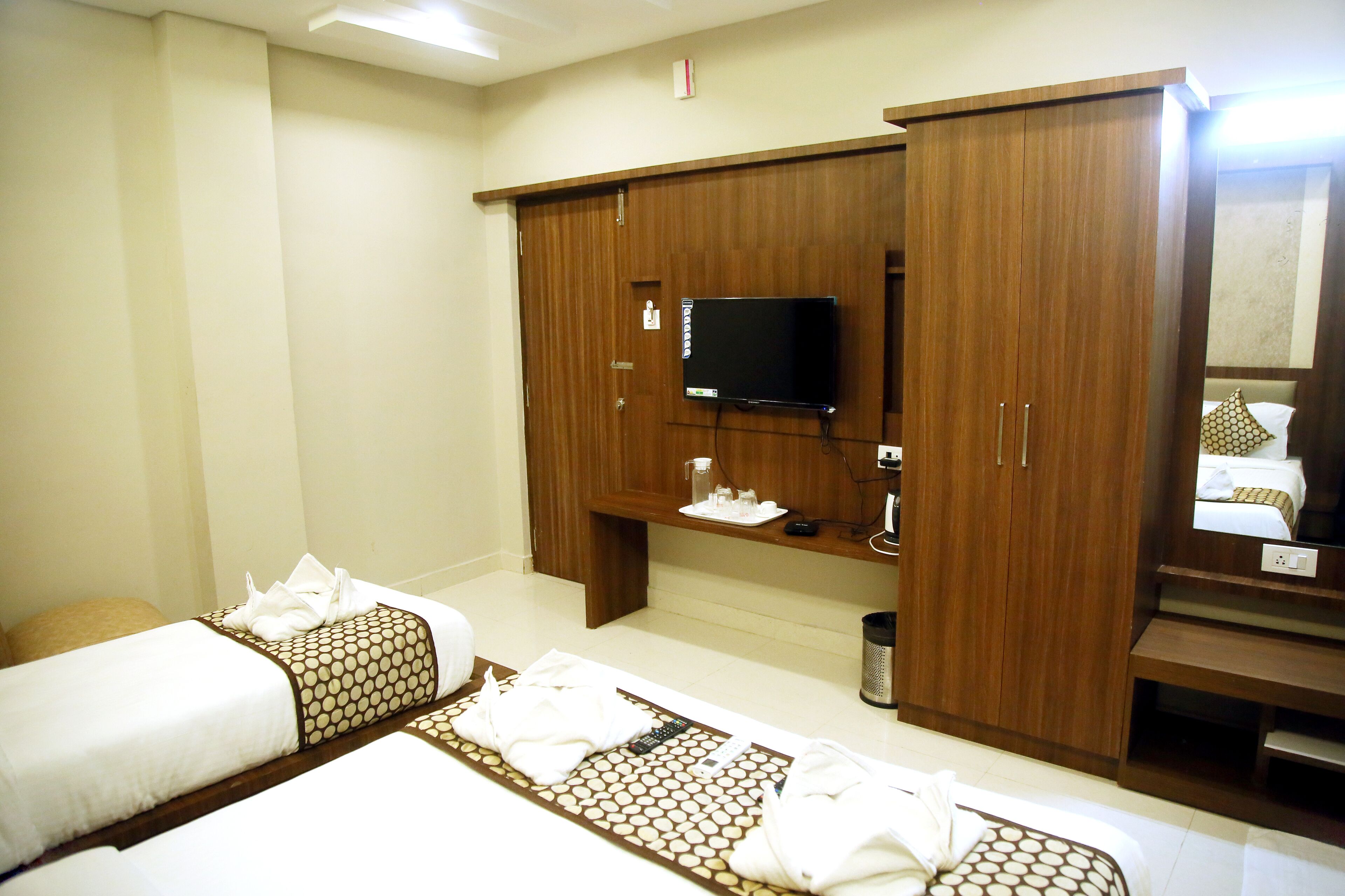 A hotel room with two beds, a TV, a wardrobe, and a small table with toiletries.
