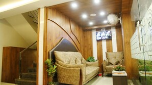 A cozy living area with a sofa, armchair, and a small table with a plant. A staircase is visible in the background. - Grand Oliver (Chennai)