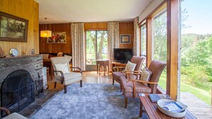 Una sala de estar acogedora con chimenea, asientos cómodos, televisión y ventanas amplias con vistas al exterior.