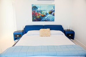 Ein Schlafzimmer mit einem großen Bett, zwei Nachttischen, einem Bild an der Wand und einem Fenster.