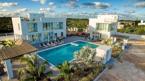 Un hotel moderno con una piscina amplia, varios balcones y un paisaje exuberante.