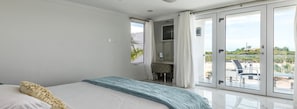 Un dormitorio con cama, escritorio y vistas a un balcón con mobiliario exterior.