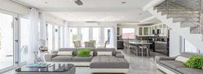 Ein modernes Wohnzimmer mit Sofa, Hocker und Couchtisch. Es gibt eine Küchenzeile mit Bar und Barhocker.