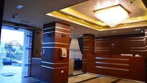 Ein Hotel-Empfangsbereich mit modernem Design, ausgestattet mit einer Rezeption, einer Kristallleuchter und einem digitalen Schild.