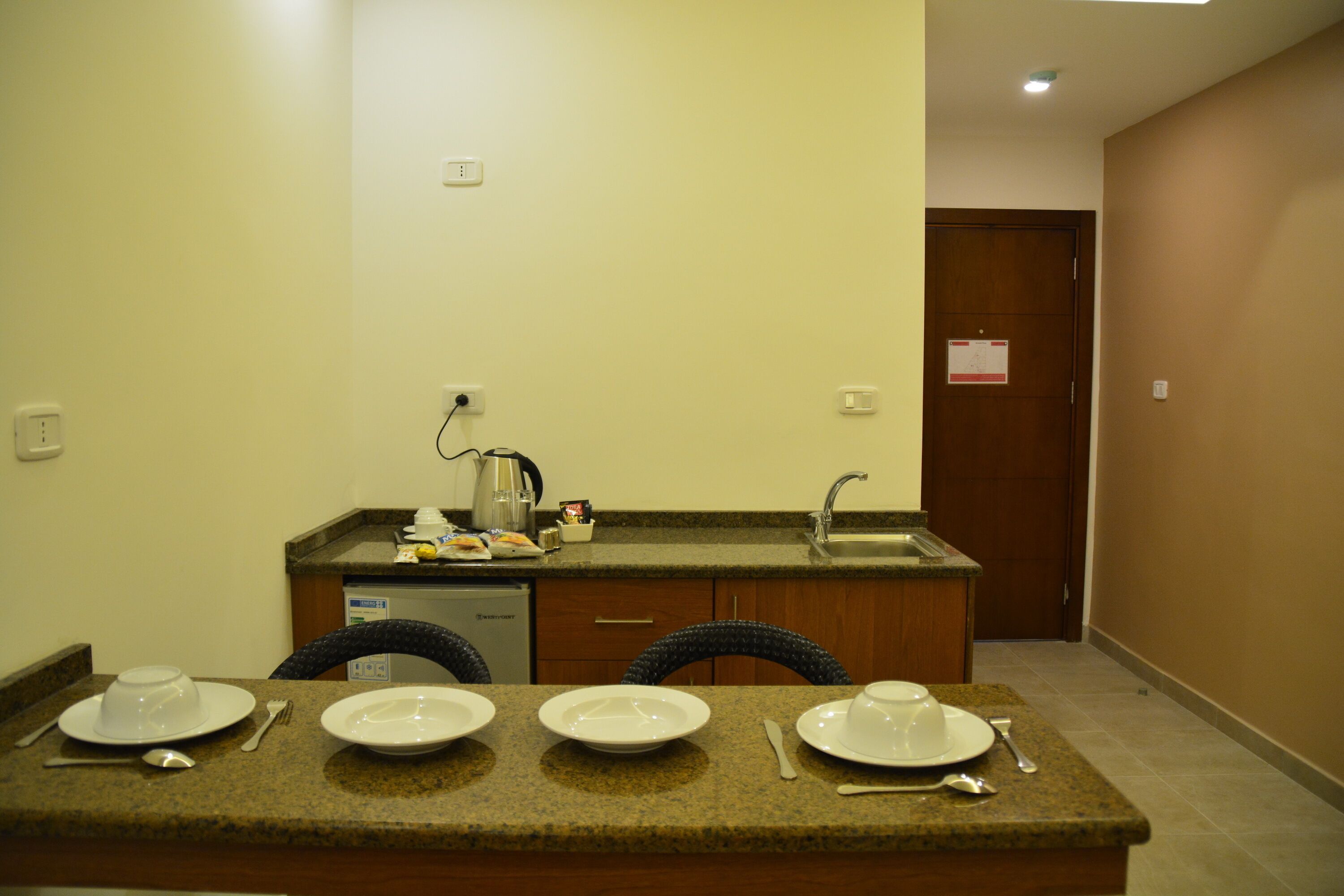 A small kitchenette with a sink, a coffee maker, and a microwave. There is a dining area with a table set for two, including plates, cutlery, and a cup.