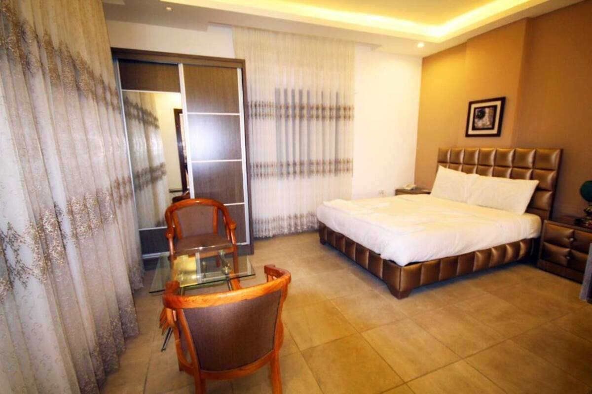 A hotel room with a bed, a desk with a chair, a wardrobe, and a window with curtains.