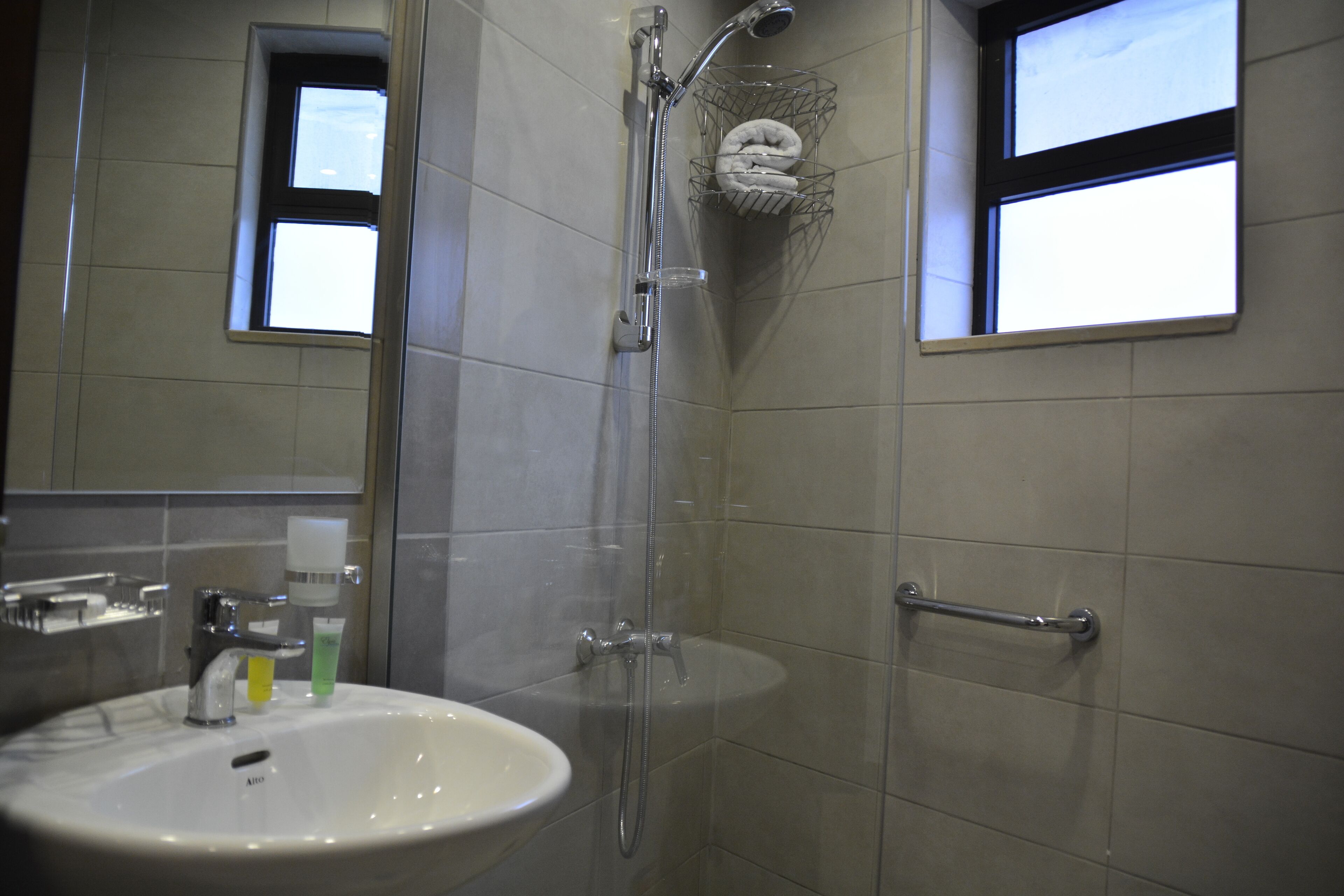 Un baño con lavamanos, espejo, ducha y toallero.