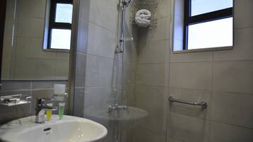 Un baño con lavamanos, espejo, ducha y toallero.