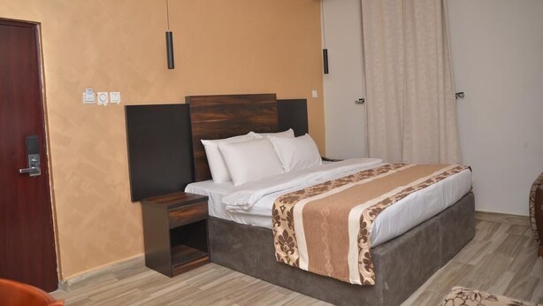 A hotel room with a bed, bedside table, and a wardrobe. - Newton Hotels Limited Owerri (Owerri)