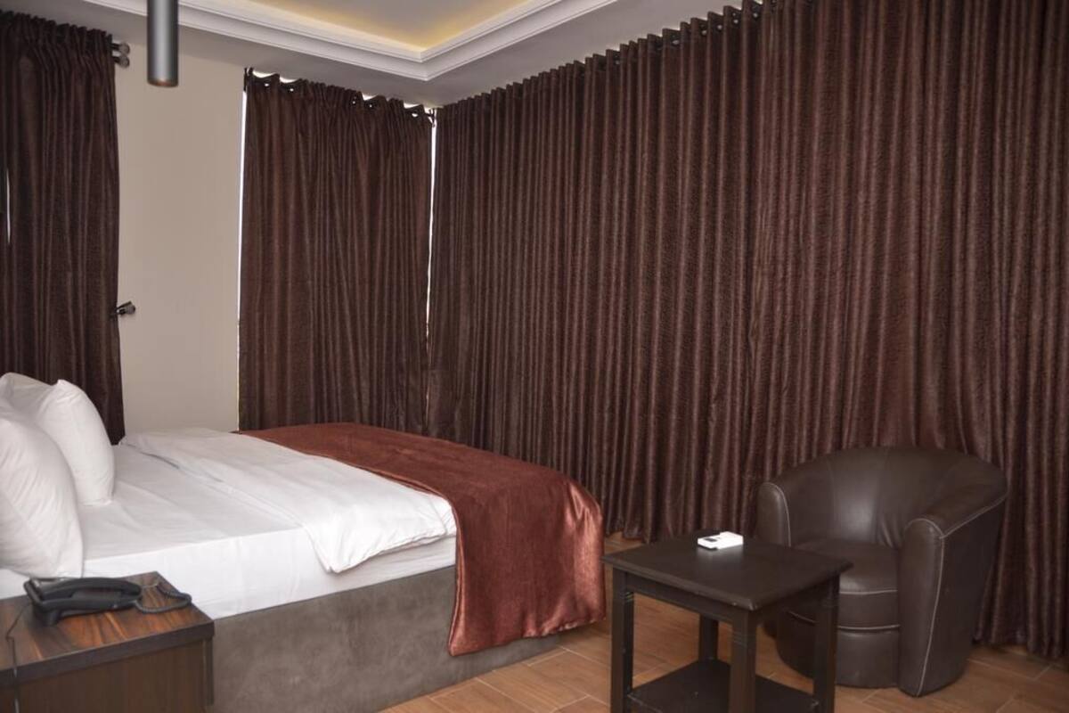 A hotel room with a bed, a chair, a small table, and a telephone on a nightstand.
