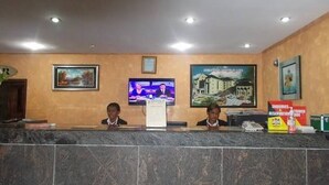 A reception area with a marble counter, two receptionists, a television, and framed pictures on the wall. - Newton Hotels Limited Owerri (Owerri)