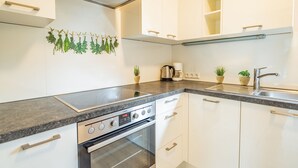 Una cocina moderna con armarios blancos, una campana extractora de acero inoxidable, horno empotrado, encimera de granito y dos plantas en macetas.