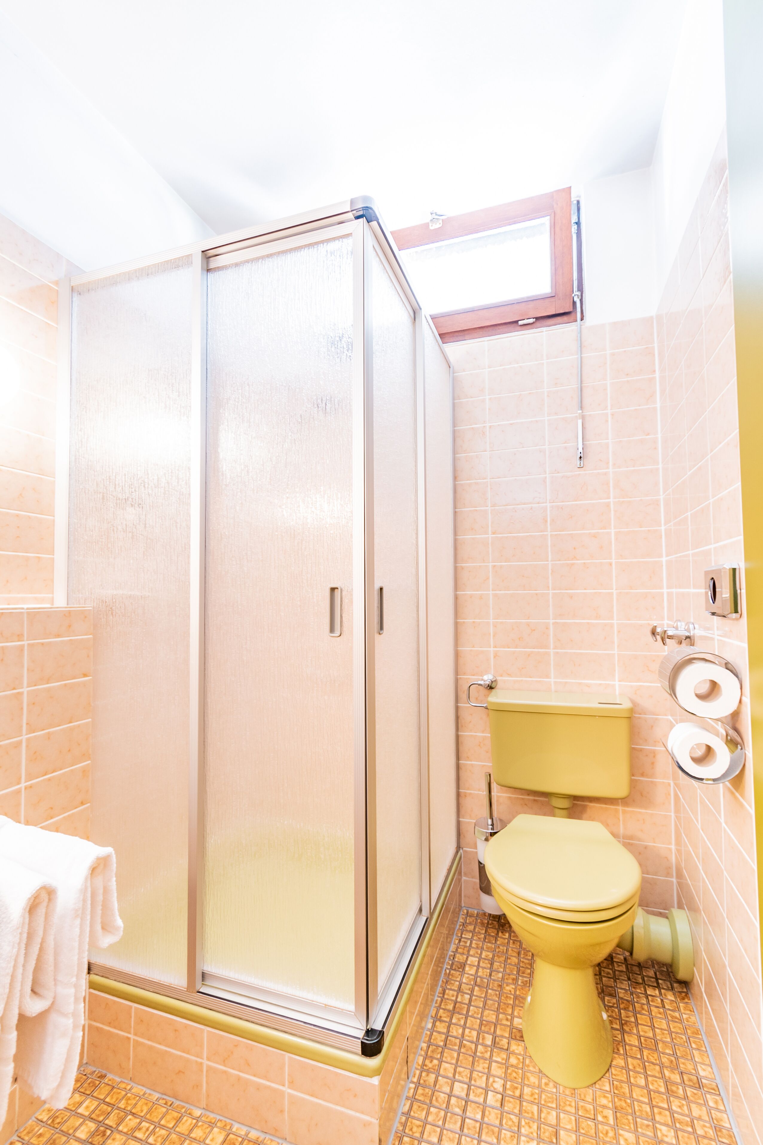 A bathroom with a glass-enclosed shower, a yellow toilet, and a towel rack.