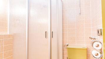 A bathroom with a glass-enclosed shower, a yellow toilet, and a towel rack.