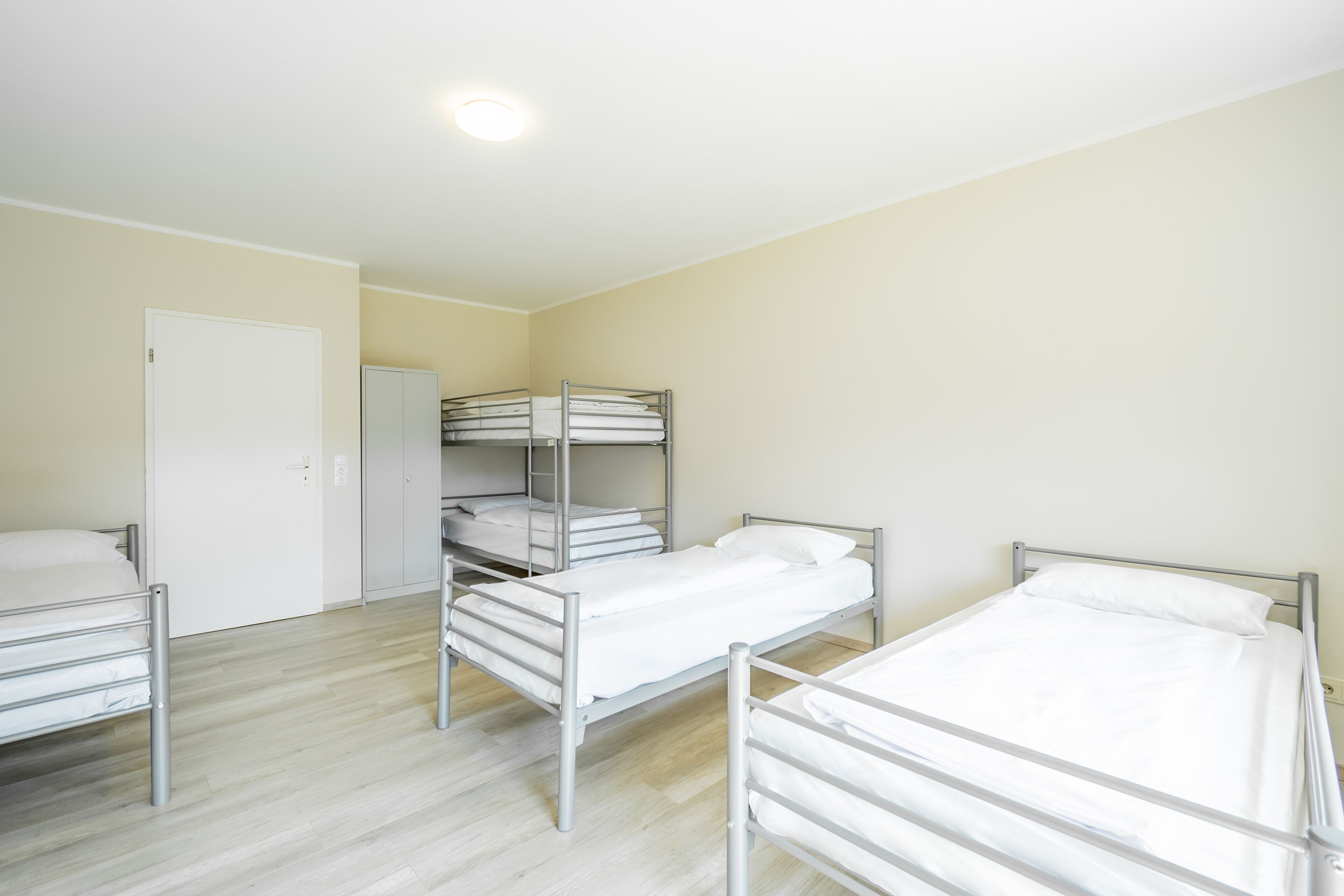 A dormitory room with bunk beds and a single bed, a white door, and a closet.