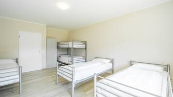A dormitory room with bunk beds and a single bed, a white door, and a closet.