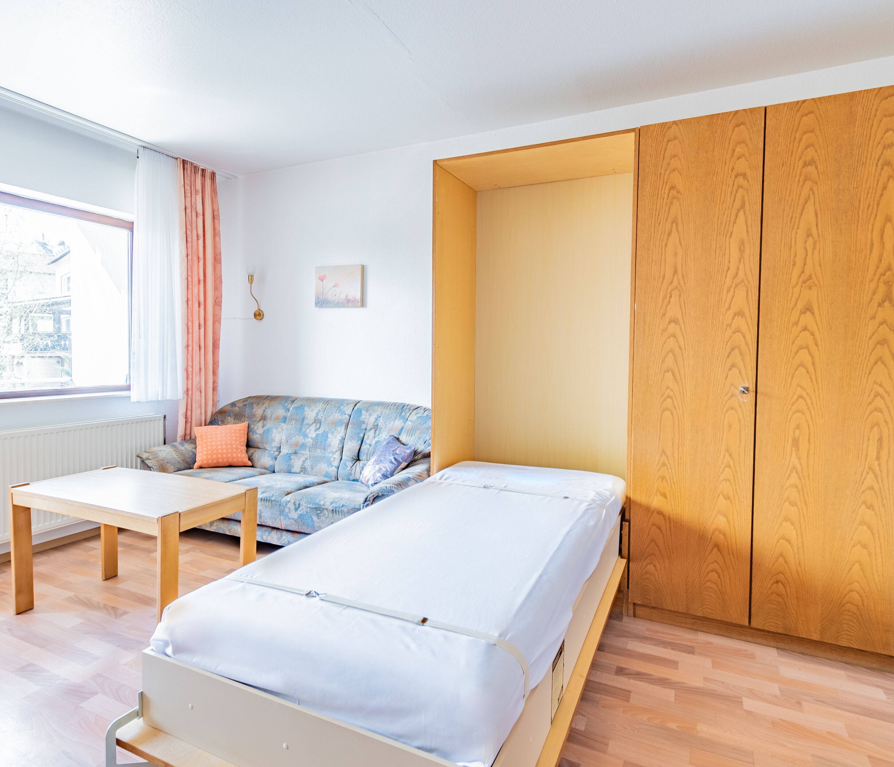 A room with a bed, a sofa, a table, and a wardrobe.