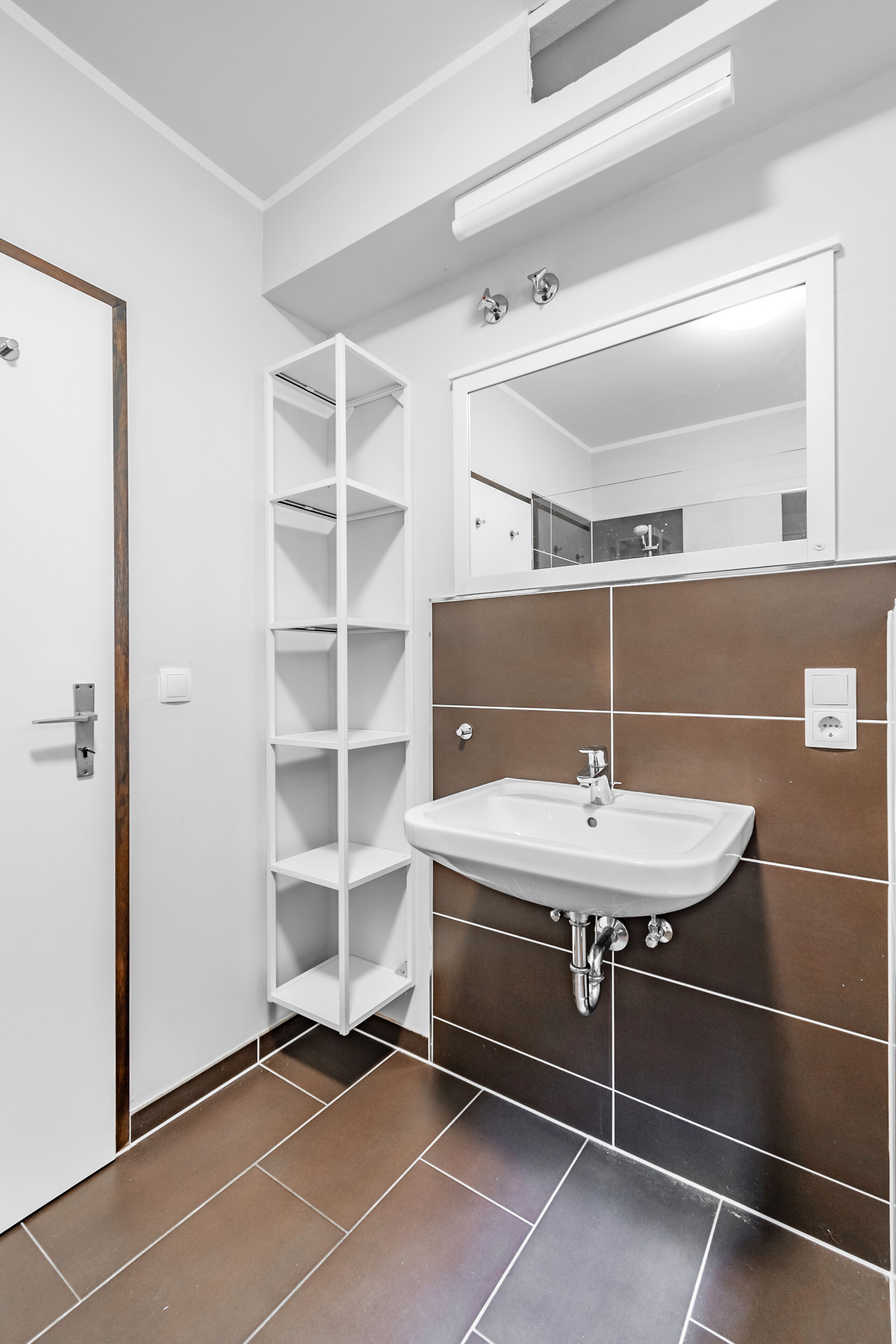 Un bagno con un lavandino bianco, uno specchio e una mensola bianca.