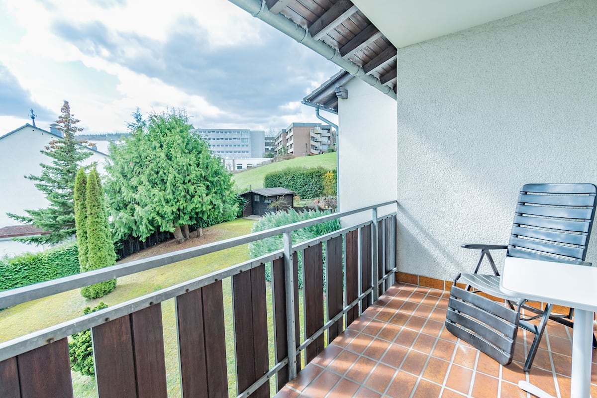 A balcony with a tiled floor, a metal railing, and a table with a chair.