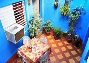 A small patio area with a table and chairs, surrounded by potted plants and a white air conditioning unit. - Hostal San Miguel TRINIDAD (Trinidad)