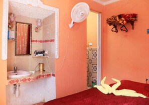 A room with a bed, a white fan, a red blanket, and a wall-mounted shelf with a decorative item. - Hostal San Miguel TRINIDAD (Trinidad)